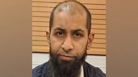 Umar Dawood police mugshot against a wood-panelled background