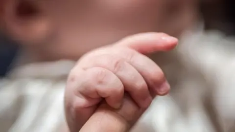 A baby holding an adult's finger