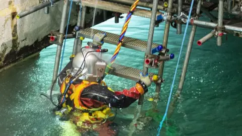 A diver climbs a ladder into a bright blue pool