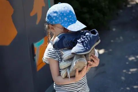 Getty Images A child precariously carrying a pile of shoes to the recycling centre