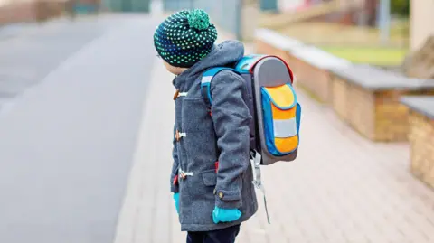 Getty Images School pupil wearing a blue coat, blue gloves and a blue hat with green dots, while stood ready to cross a road.