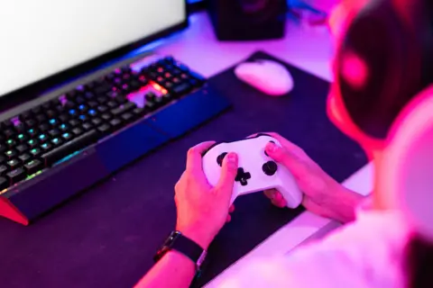 Getty Images Seorang gamer memegang gamepad dan memainkan video game di desktop