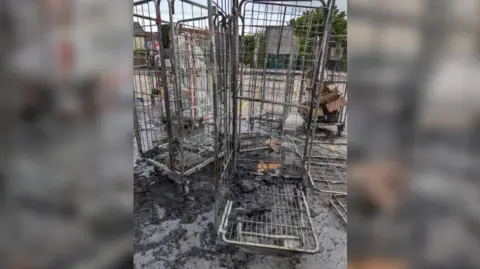 Wiltshire Police Tall metal cages on wheels usually used to take products around a supermarket with charred remains of boxes and ash around them.