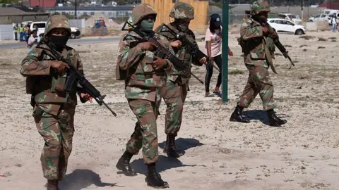 Four uniformed soldiers are seen walking through a Cape Town township as part of their deployment to the area
