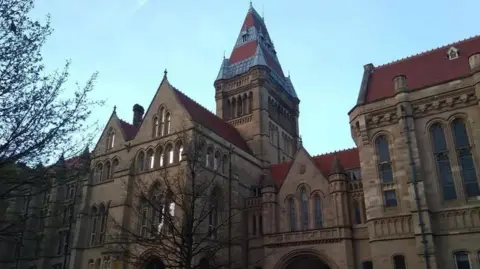 The spires of a stone university building loom towards the sky on a clear day.