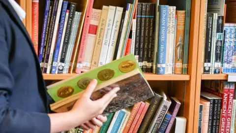 Child's hands holding a book with library shelves visible behind