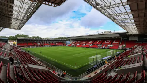 A long-range shot of Ashton Gate stadium, pictured from the upper right hand corner of one of the stands. A football pitch is set up in the middle, and the word 'Bristol' is spelt out in white seats amid blocks of red seats.