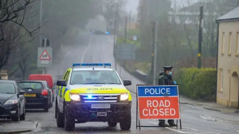 police at the scene of the alert with a road closed sign