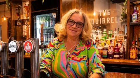 Miranda Richardson Miranda Richardson wearing a multi coloured shirt smiling at the camera as she stands behind her pub bar next to an Aspall and Madri beer tap with lots of spirit bottles behind her on a counter