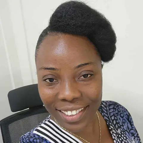 A selfie of Henrietta Peters Magbollah. She's smiling and wearing a blue floral dress with her hair in a large bun
