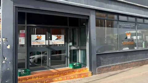 Help the Homeless Front of a building with two doors with sign on the doors and window