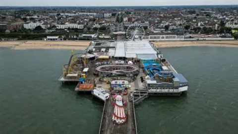 Getty Images The pier at Clacton from above. The helter skelter and various other attractions are visible, including the ferris wheel. In the foreground is the beach and buildings near the shore.