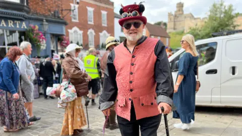 Amber Macey/BBC Man dressed in red-speckled waistcoat with a red top hat and goggles