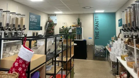 A number of refill stations can be seen holding different herbs and foods. In the background there is a blue wall with 'The Pantry' written on it.