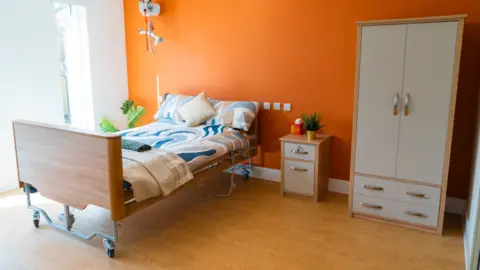 Surrey County Council A bedroom, a bedside table and a wardrobe in a room at Emily Lodge.
