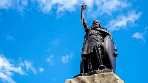 Getty Images Statue of King Alfred the Great in Winchester, England, holding a sword pointing downwards aloft in his hand.