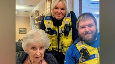 West Midlands Police Two police officers, a man and woman smile at the camera next to an elderly woman who is also looking at the camera