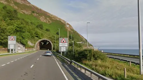 Google A dual carriageway by the sea with one direction going into a tunnel