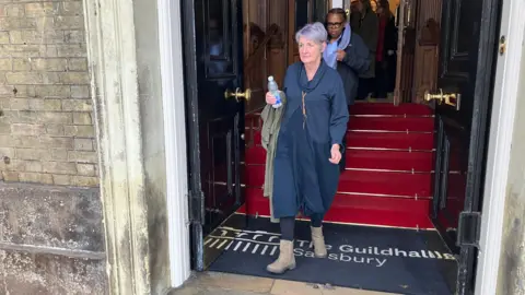 Caroline Sturgess wears a navy bluish  dress. She is walking retired  of Salisbury Guildhall