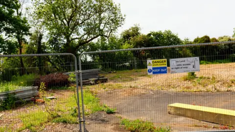 Mark Ashdown Metal temporary fencing in front of wasteland covered in scrub. A sign on the gate reads "Private land. No public access or right of way". 