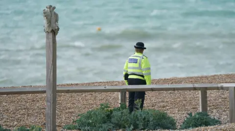 PA Media A lone police officer stood on a beach facing away from the camera towards the sea
