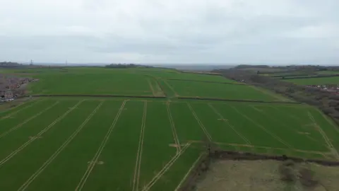 An aerial photo of fields, showing a housing estate on the left and the right of the photo

