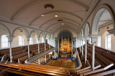 RCAHMW Interior view of Zion Baptist Chapel, looking from front to back of the church to the wooden pulpit and golden pipe organ surrounded by wooden pews and beneath an arched roof