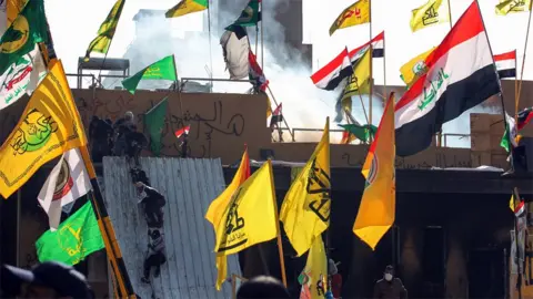 AFP Supports of Iraqi militias climb onto the outer walls of the US embassy in Baghdad during a protest on 1 January 2020