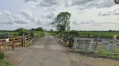 A level crossing on an isolated rural road. The crossing is open and surrounded by fences and gates. 