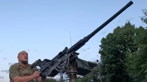 MOOSE CAMPBELL/BBC Unit commander Jaeger holds a machine gun pointed towards the sky