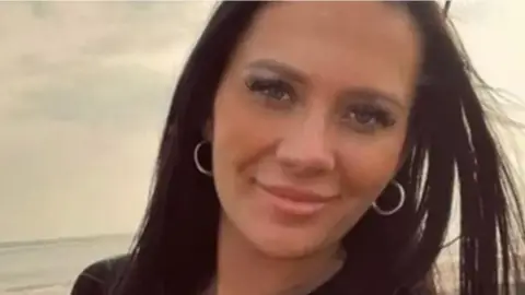 Head and shoulders image of Kiena Dawes on a beach, she has long straight dark hair and is smiling