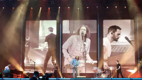 Getty Images Snow patrol performing on a stage with a large screen behind them. 