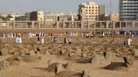 Getty Images Unmarket graves in Al-Baqi Cemetery, with people walking around the grounds