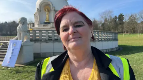 Deborah Lewis: A woman with red hair wearing a yellow top, black jacket and yellow hi-vis vest