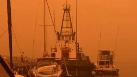 Reuters An orange sky shrouds boats at a wharf in Eden, NSW