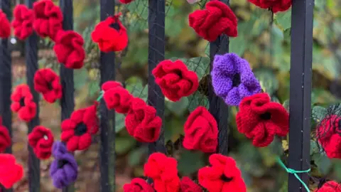 Getty Images Close-up of homemade knitted poppies attached to an iron fence outdoors in nature for Remembrance Sunday.