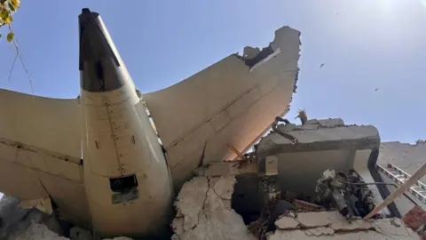 The tail of the plane sticks out from the building it crashed into, men in military uniform have accessed an upper floor of the partially collapsed building.