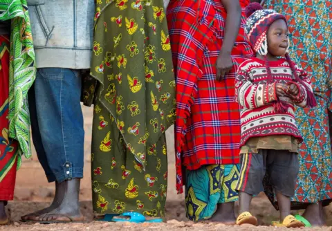 Reuters A boy wearing a knitted hat and jumper stands next to a line of adults wearing clothes in various patterns.