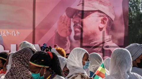 AFP A poster with Prime Minister Abiy Ahmed wearing army uniform. There are people walking past it, one with an Ethiopian flag.