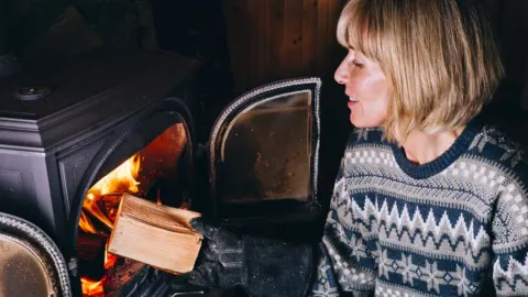 Getty Images Woman putting logs in a wood burning stove - stock photo