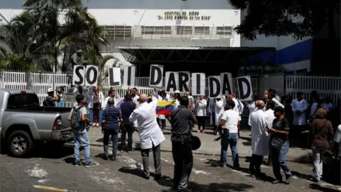 Reuters Venezuelans, including doctors, hold banners that read "Solidarity" as they gather outside a public children hospital during an ongoing blackout in Caracas, Venezuela March 10, 2019.
