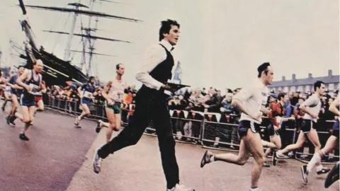 Supplied Roger Bourban wearing a waiter's suit and carrying a tray as he runs the London Marathon