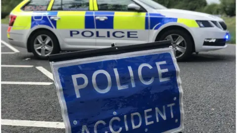 A police car parked next to a sign that reads: POLICE - ACCIDENT