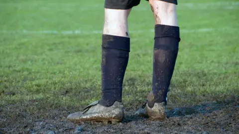 A football player stood on a muddy pitch