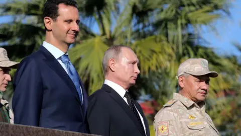 EPA Syrian President Bashar al-Assad (L), Russian President Vladimir Putin (C), Russian Defence Minister Sergei Shoigu (R) visit the Hmeimim airbase in Syria (11 December 2017)