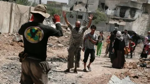 Reuters Iraqi man holds his hands up for a security check in Mosul (June 2017)