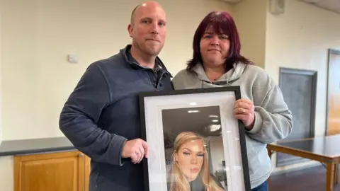 Ben Branson (left) and Amy Branson (right) holding a framed photo of Bethany