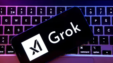 A smartphone with the XAI and Grok logo on screen sits on top of a laptop keyboard, lit by purple lighting