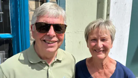 Ben Parker/BBC A man is on the left with a pale green top on, he is wearing sunglasses, on the right is a woman wearing a blue top, they are both looking at the camera.