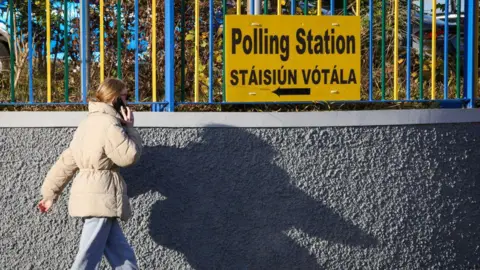 Getty Images A pistillate   successful  a beige overgarment  and grey trousers walks past   a yellowish  motion   connected  a obstruction   that says 'Polling Station' successful  English and Irish.